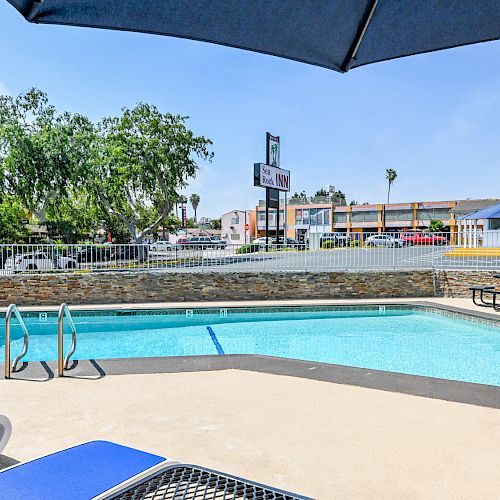 This image shows an outdoor pool area with lounge chairs, a picnic table under an umbrella, and a Pepsi machine in the background.