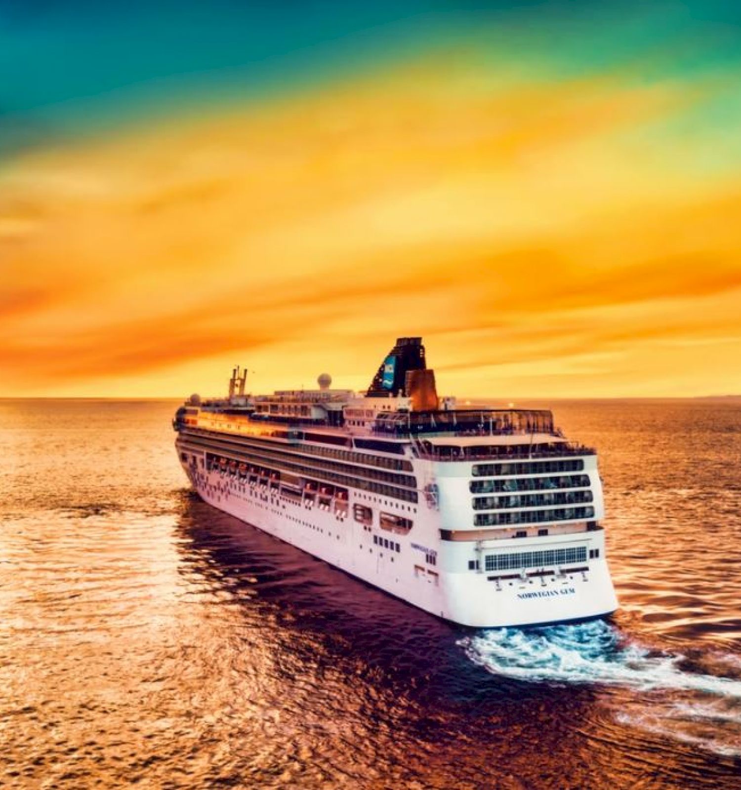 A large cruise ship sails on the ocean under a vibrant, colorful sunset sky, leaving a wake behind it across the calm water.