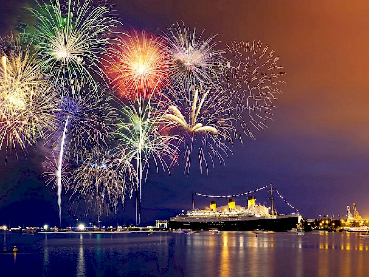 A grand display of colorful fireworks illuminates the night sky above a large ship docked at a peaceful harbor.