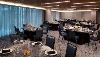 The image shows an elegant banquet hall setup with round tables, each covered with black tablecloths, set for dining with plates, glasses, and folded napkins.
