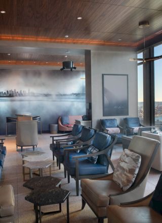 This image depicts a modern lounge area with comfortable seating, large windows offering an ocean view, and a mural on the back wall.