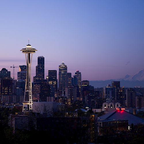 The image shows the Seattle skyline at dusk with the iconic Space Needle and Mount Rainier in the background, under a serene evening sky.