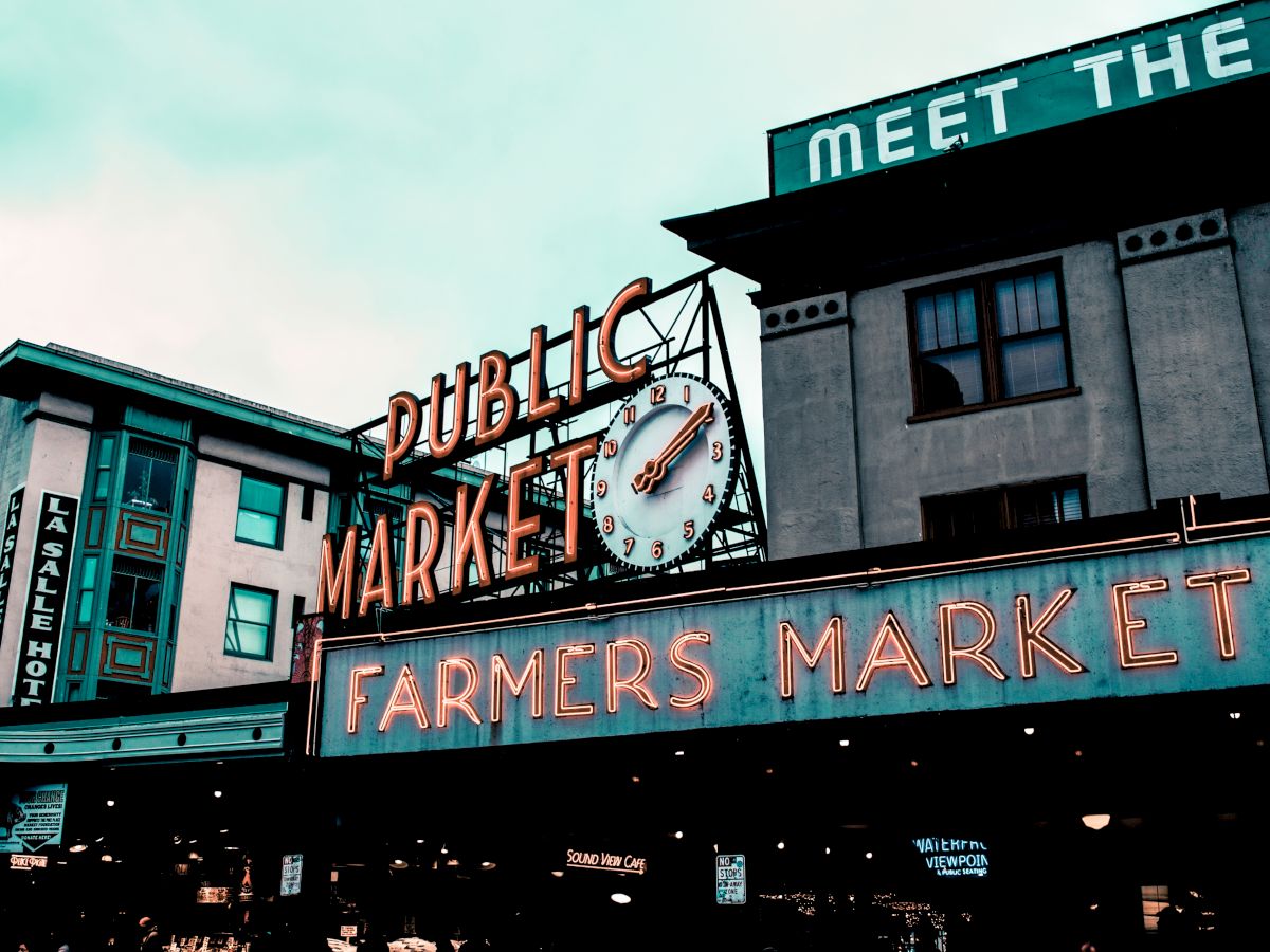 The image shows the iconic signage for a public market and farmers market, with a clock, located on buildings in an urban setting.