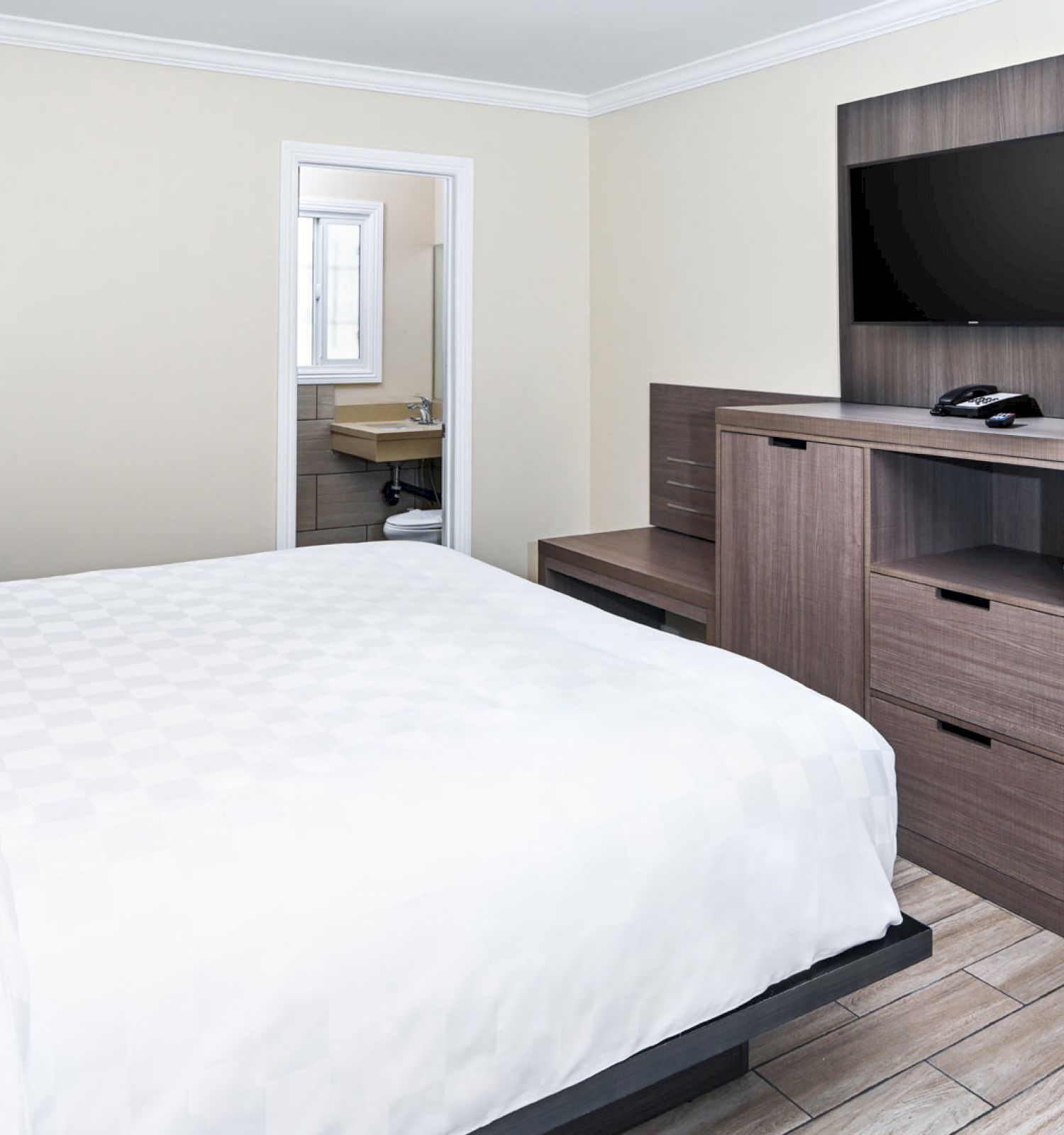 A hotel room with a bed, desk, TV, chair, dresser, and open closet, with a glimpse of the bathroom visible in the background.